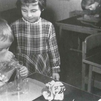 The little boy is very deliberately and carefully pouring water from one container into another, trying to avoid spilling any. He practises distributing the liquid into different containers, into wide and narrow openings. Soon he will be able to pour drinks from any container at all, or water the plants. Berlin Children's House, 1961 - T. Müller, R. Schneider, <em>Lehrmaterialien 1913-1935. Möbel und Architektur. Techning Meterials 1913-1935. Furniture and Architecture</em>, München, Prestel Verlag, 2002, p.81$$$424