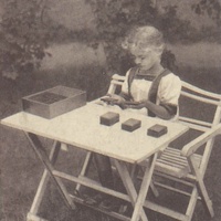 Girl judging the weight of the baric sense tablets, Children's House, Berlin-Lankwitz 1919-22. Postcard published by the DMG (German Montessori Society), around 1927, with the inscription: "If a child has worked - even for a long time - at an exercise he has chosen freely we find that he is happy and relaxed afterwards, not exhausted." Photograph: Clara Grunwald - T. Müller, R. Schneider, <em>Lehrmaterialien 1913-1935. Möbel und Architektur. Techning Meterials 1913-1935. Furniture and Architecture</em>, München, Prestel Verlag, 2002, p.94$$$456